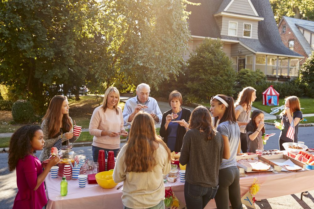 Neighbours talk and eat around a table at a block party;