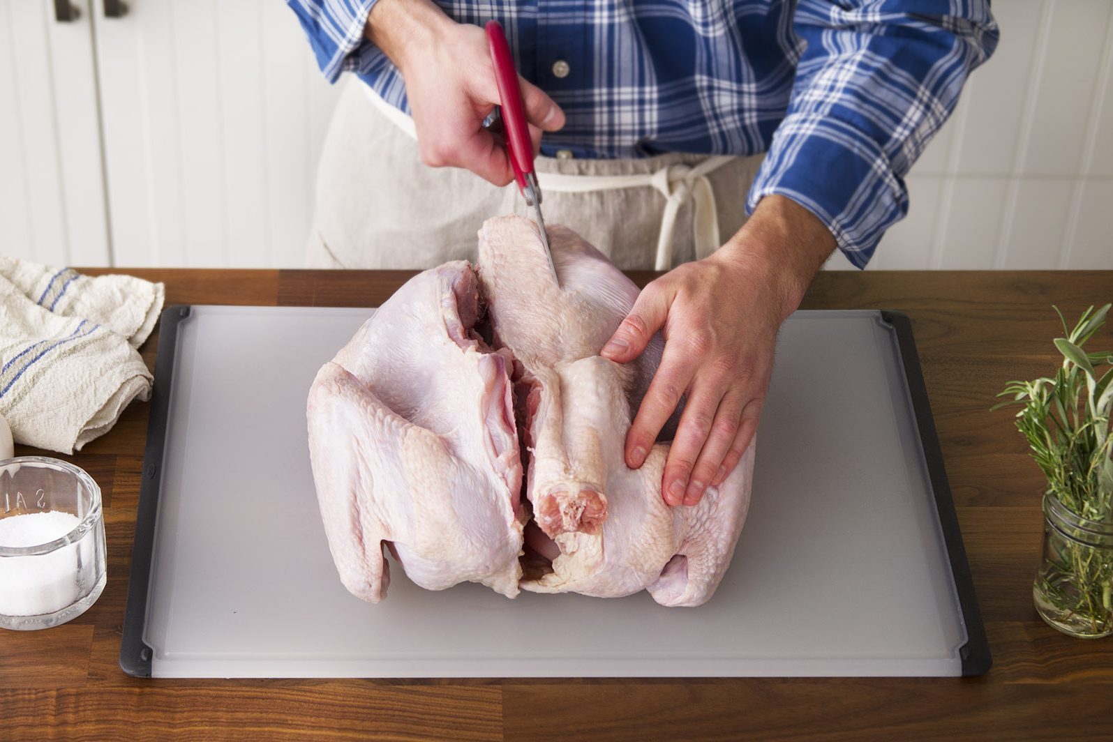 Person cutting the backbone out of a raw turkey carefully on a cutting board