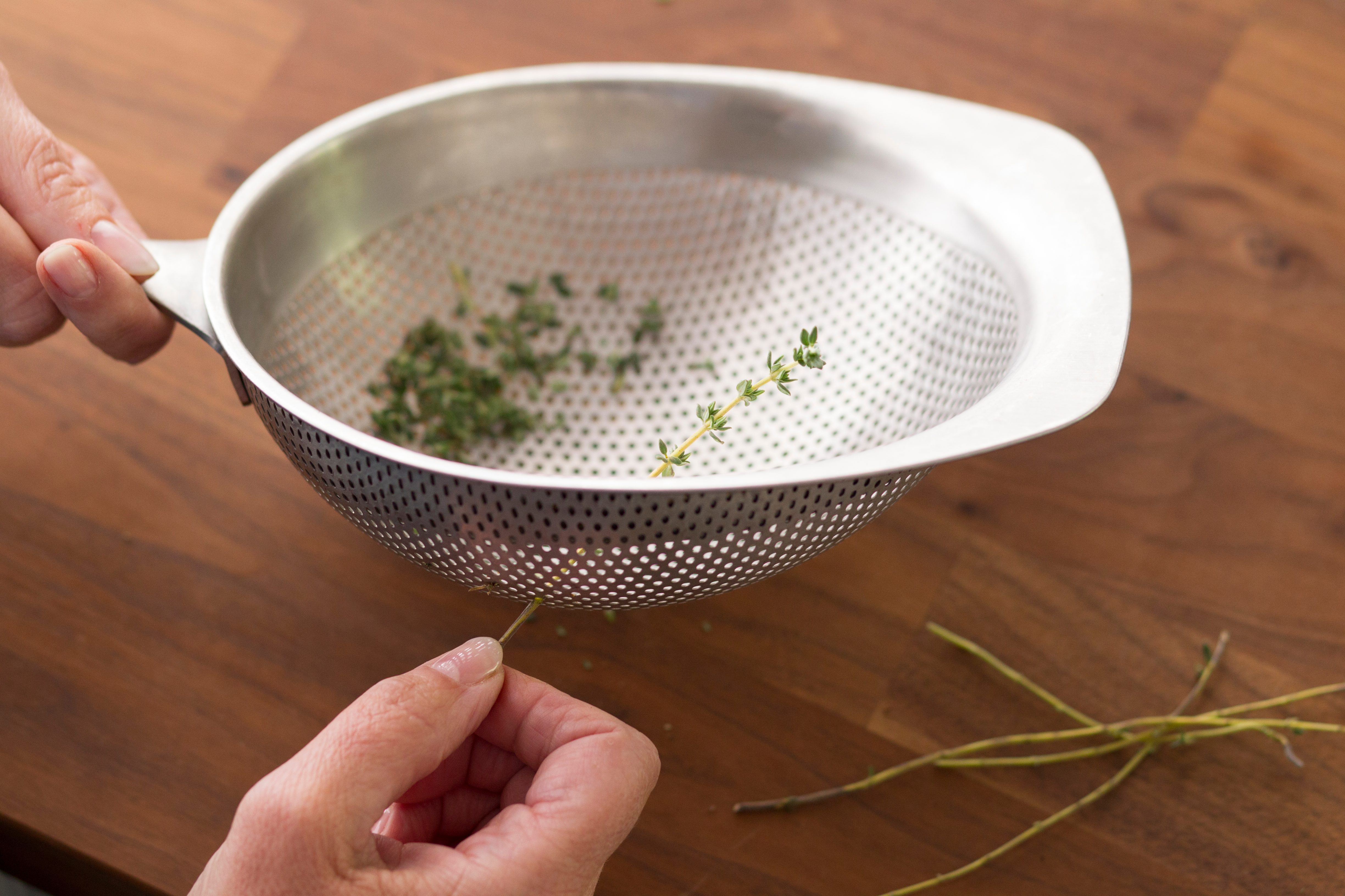 Person pulling a herb through the holes of a strainer to remove its leaves