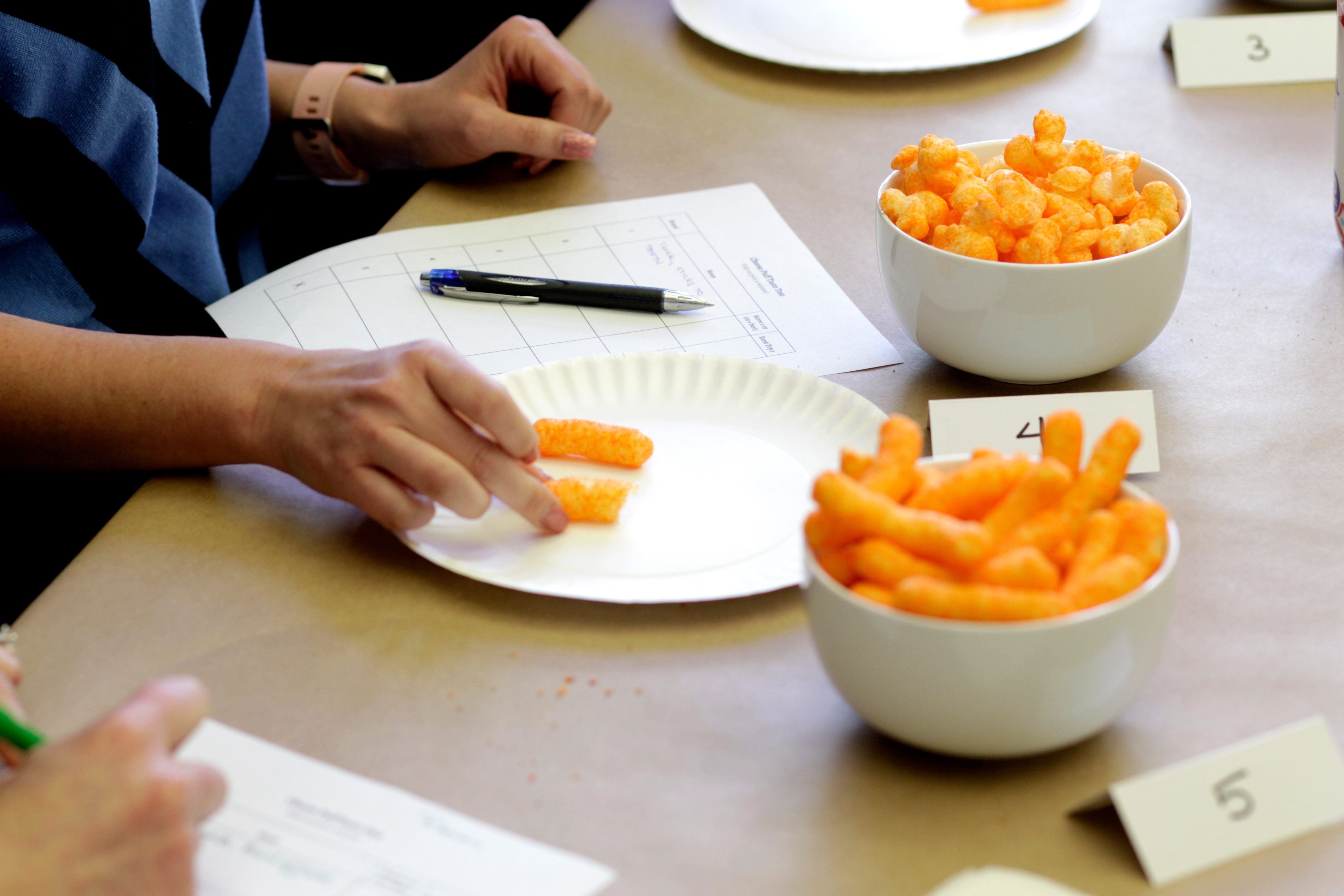 People grabbing cheese puffs from bowls as they take notes