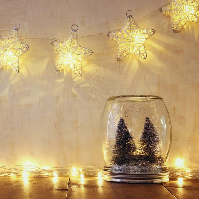 low key and vintage filtered image of christmas trees in mason jar with garland warm lights. selective focus