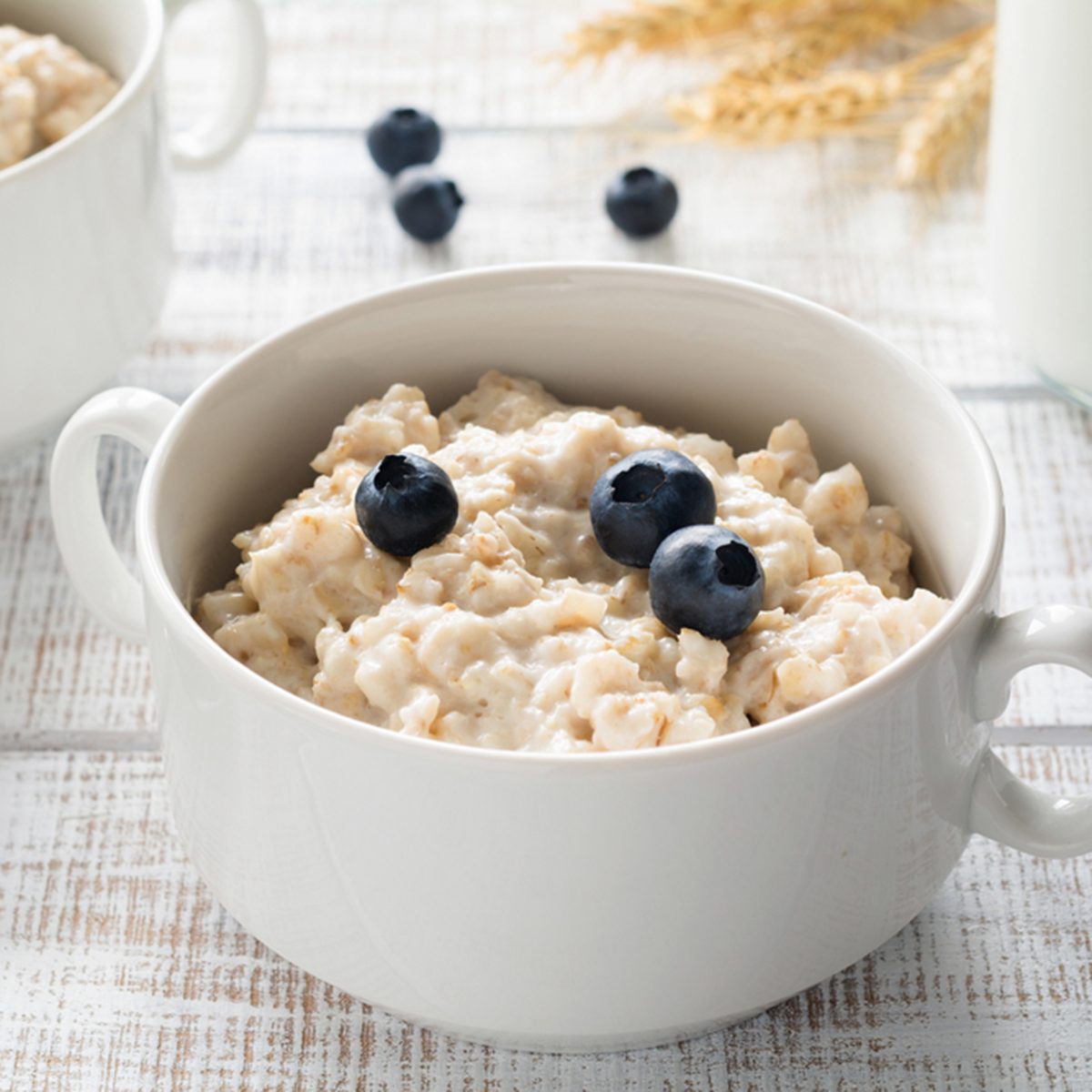 Oatmeal porridge / porridge oats / breakfast cereals with blueberries and bottle of milk on vintage white wooden table. Healthy eating, healthy breakfast food ; Shutterstock ID 644620840