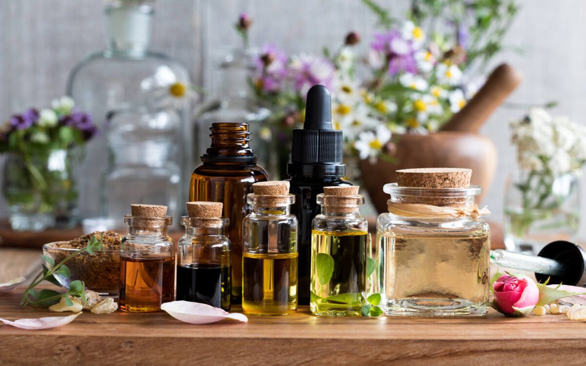 Selection of essential oils, with herbs and flowers in the background