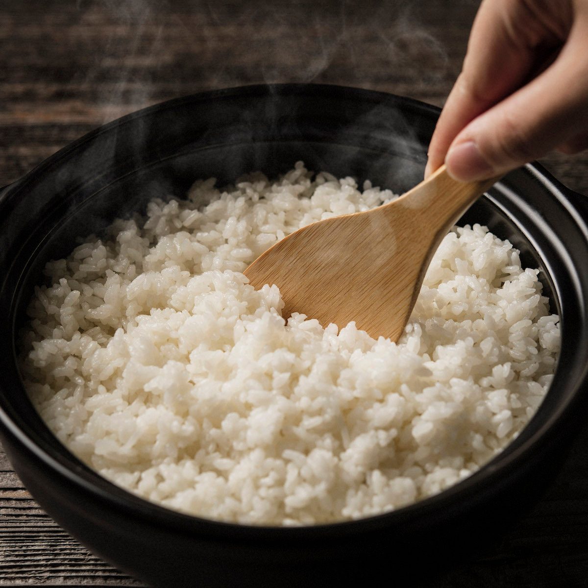 A person fluffing a pot of cooked white rice with a wooden rice paddle.