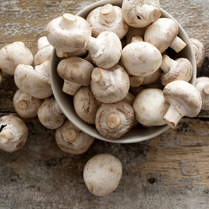 Fresh whole white button mushrooms, or agaricus, in a bowl on a rustic wooden counter ready to be cleaned and washed for dinner, overhead