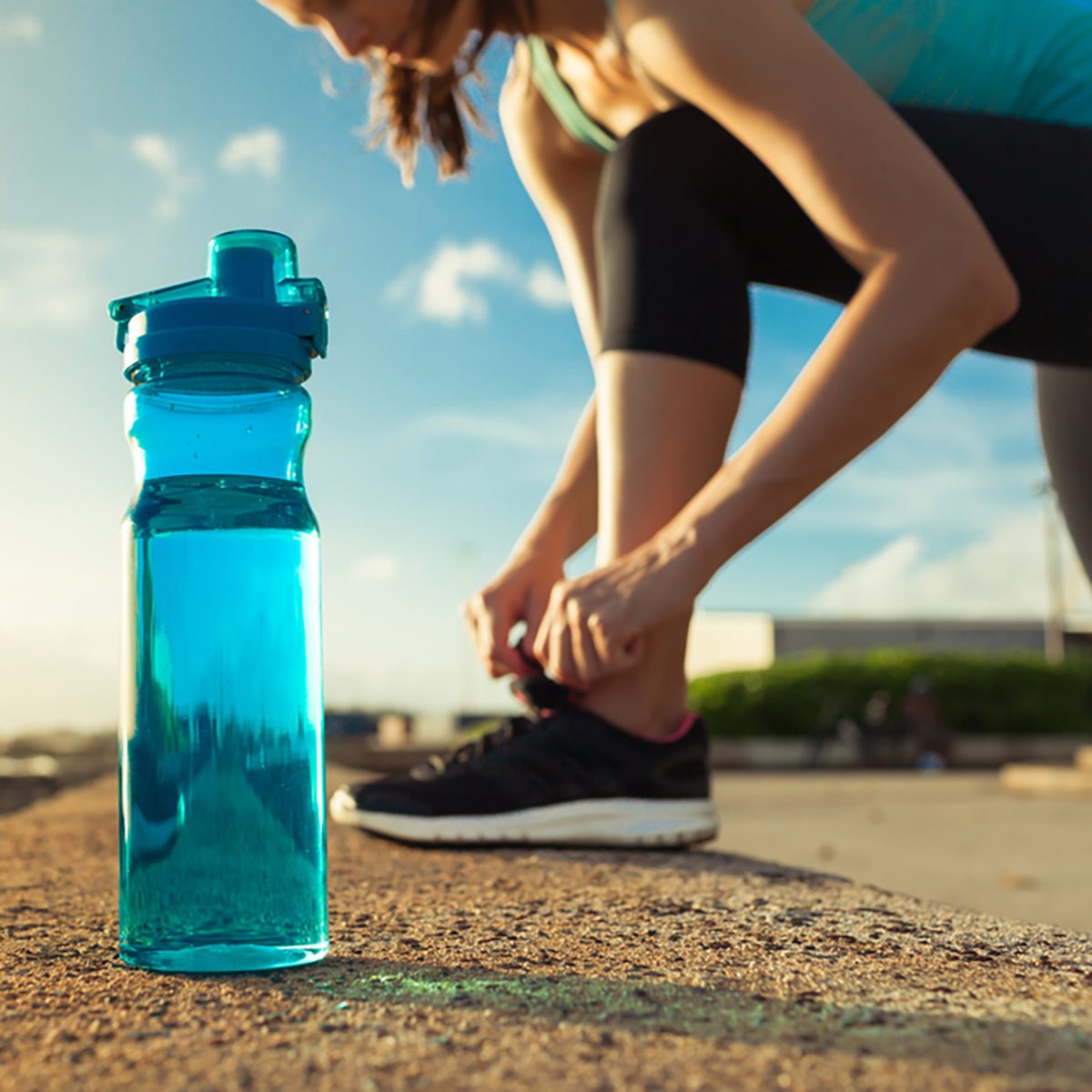 Female runner tying her shoe next to bottle of water.