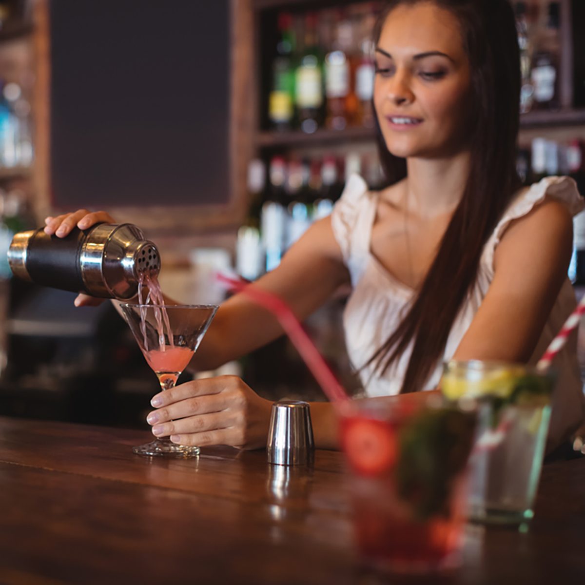Female bartender pouring cocktail drink in the glass at bar counter
