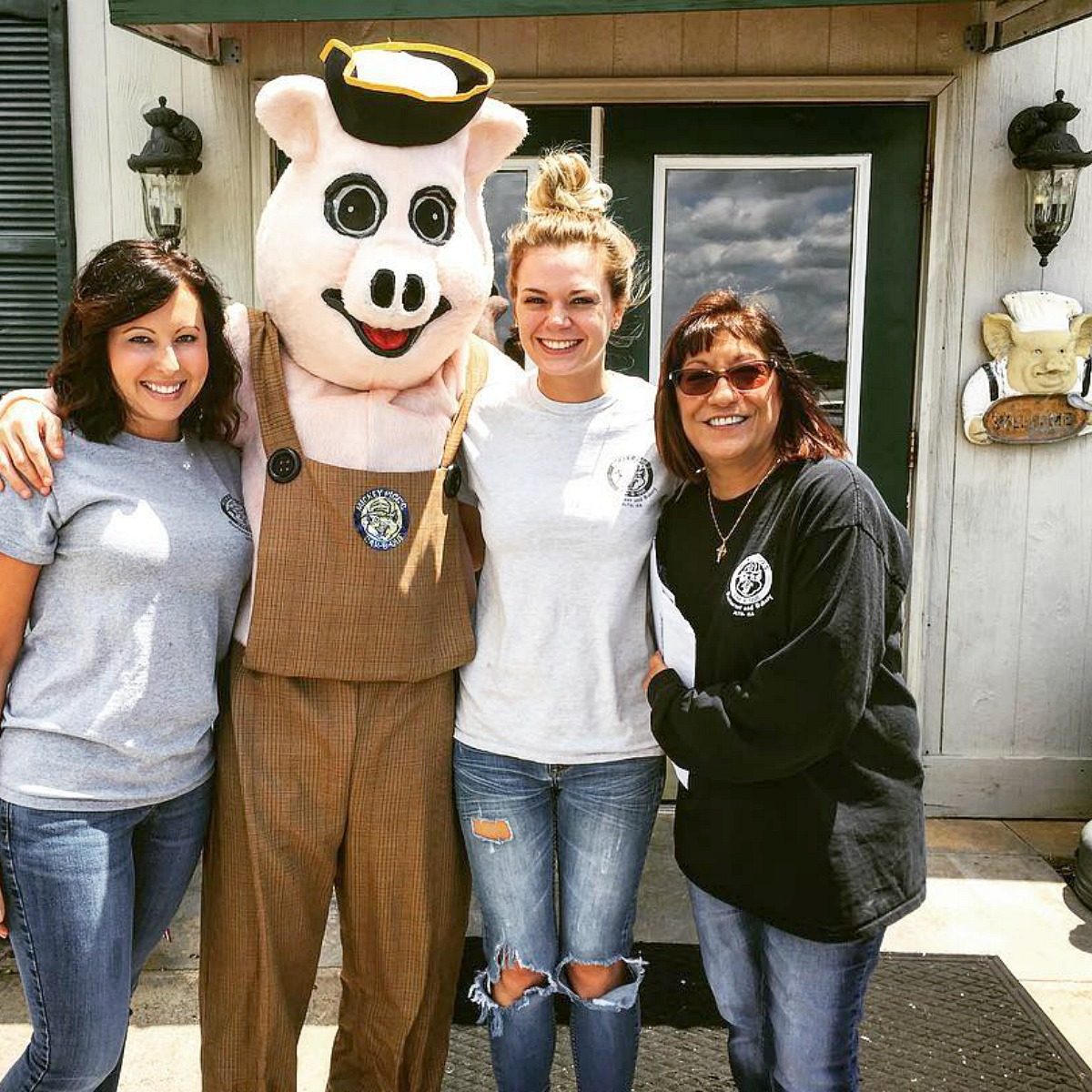 People posing with the mascot of Mickey Piggs BBQ