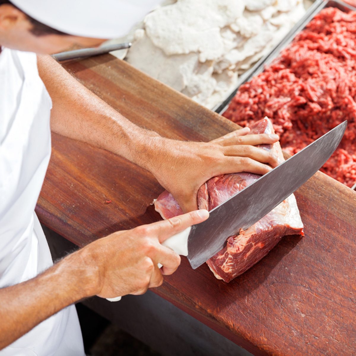 High angle portrait of smiling butcher cutting meat at counter in butchery