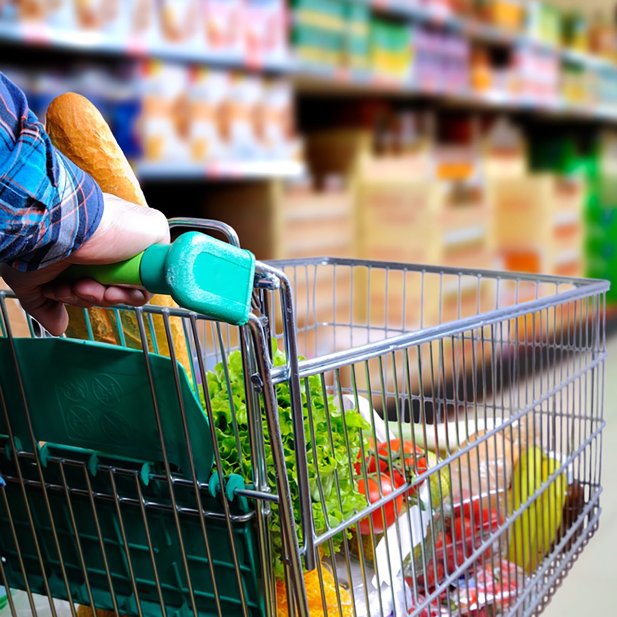 Man pushing shopping cart full of food in the supermarket aisle.