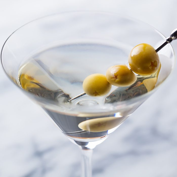 Martini cocktail with green olives on marble board.