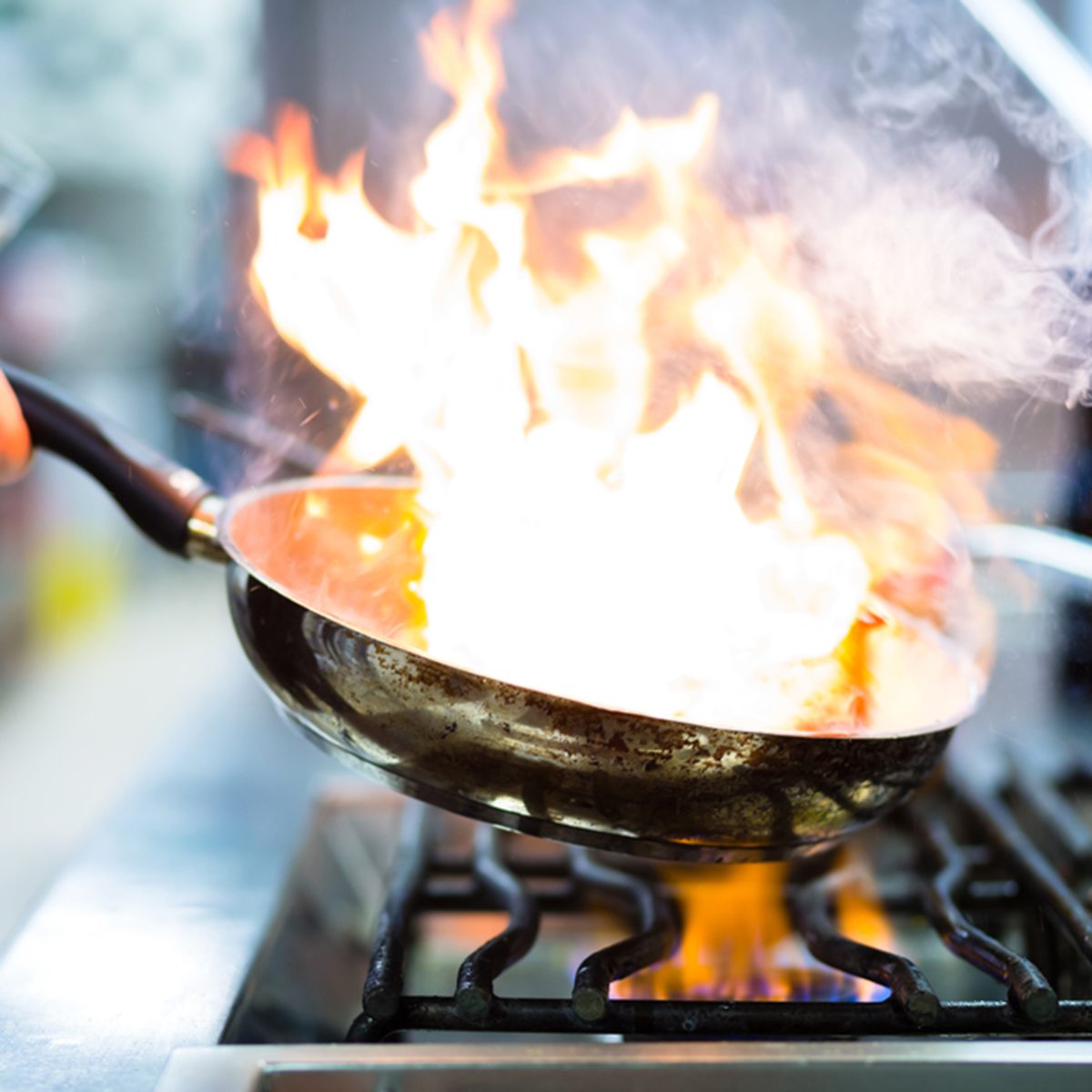 Chef in restaurant kitchen at stove with pan, doing flambe on food