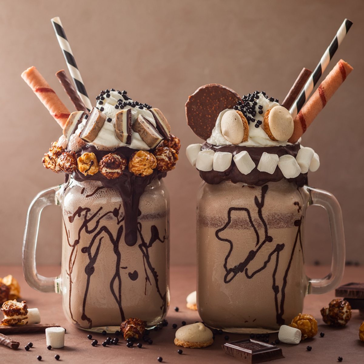 Chocolate milkshake with ice cream and with whipped cream, marshmallow, sweet popcorn, cookies, waffles, served in glass mason jar. 