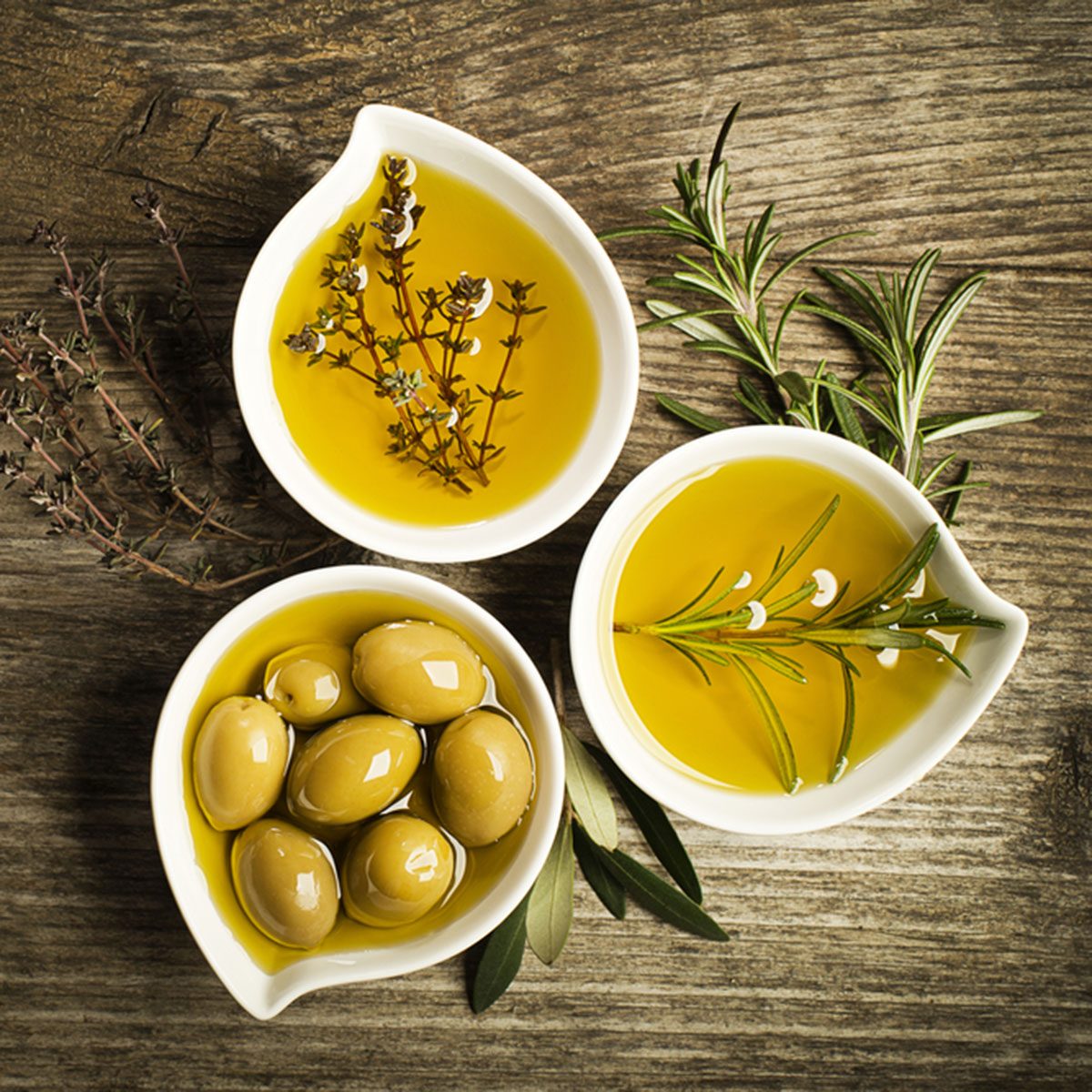 Olive oil with fresh herbs on wooden background.