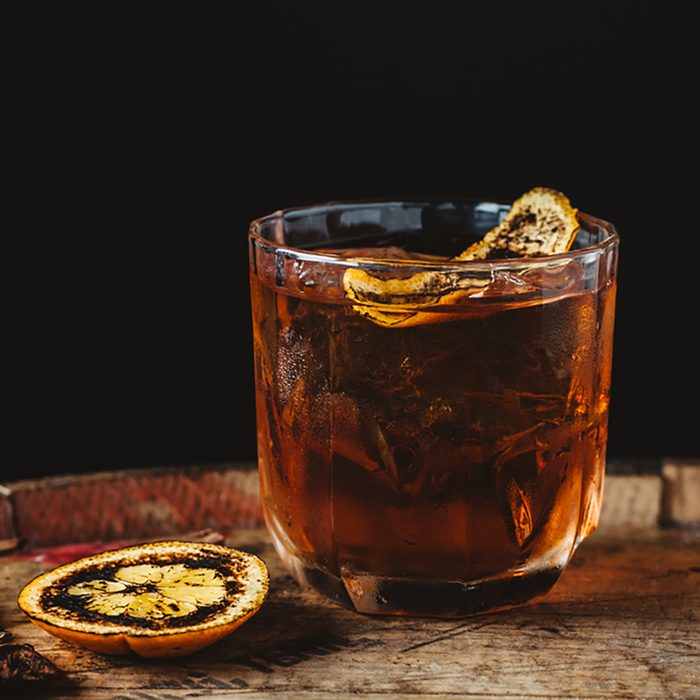 Smoked old fashioned cocktail garnished with an orange peel on dark wooden background