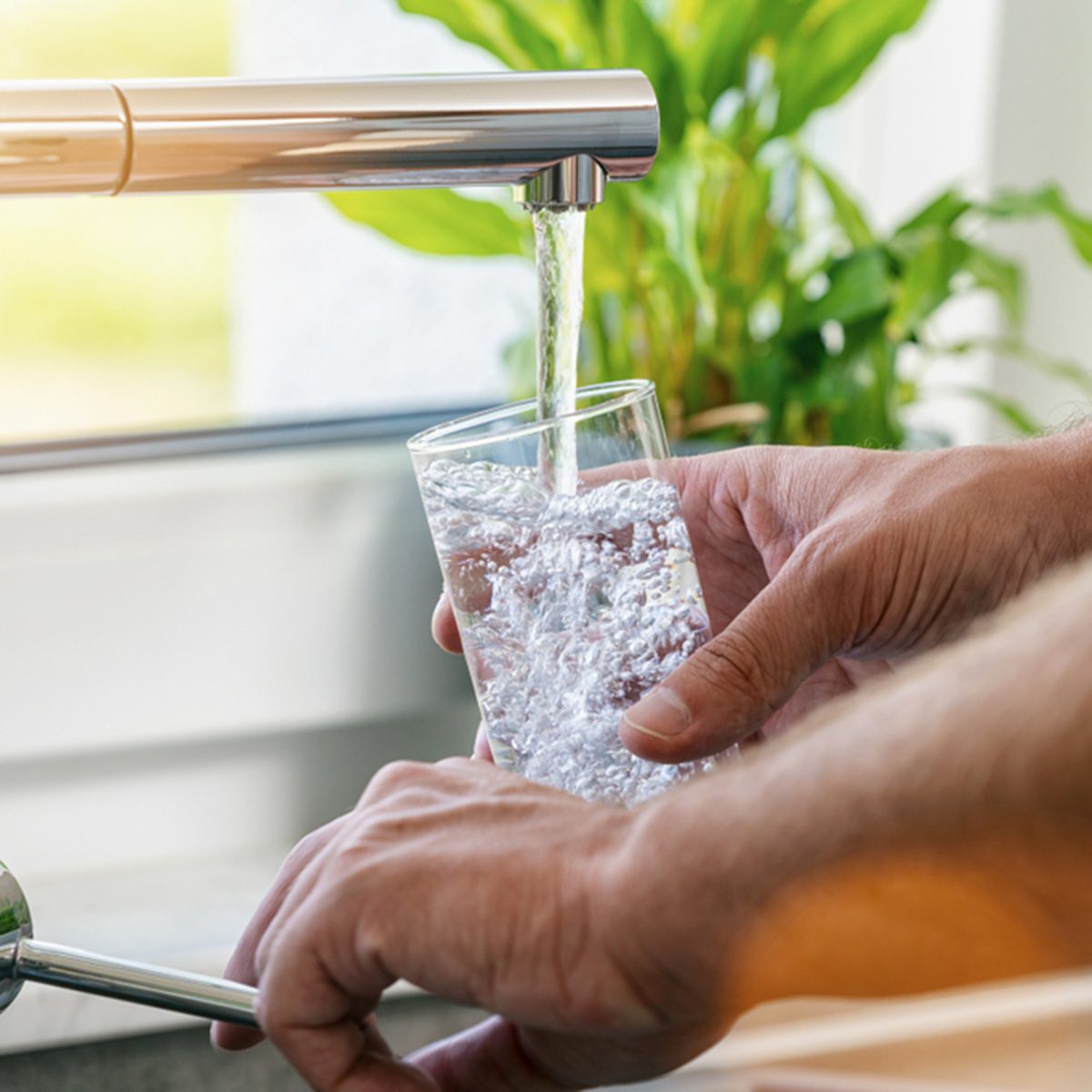 Hand holding a glass of water poured from the kitchen faucet