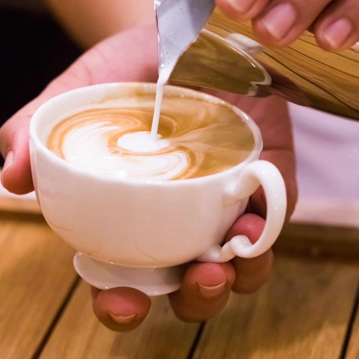 Cup of coffee with cream and coffee beans on wooden background