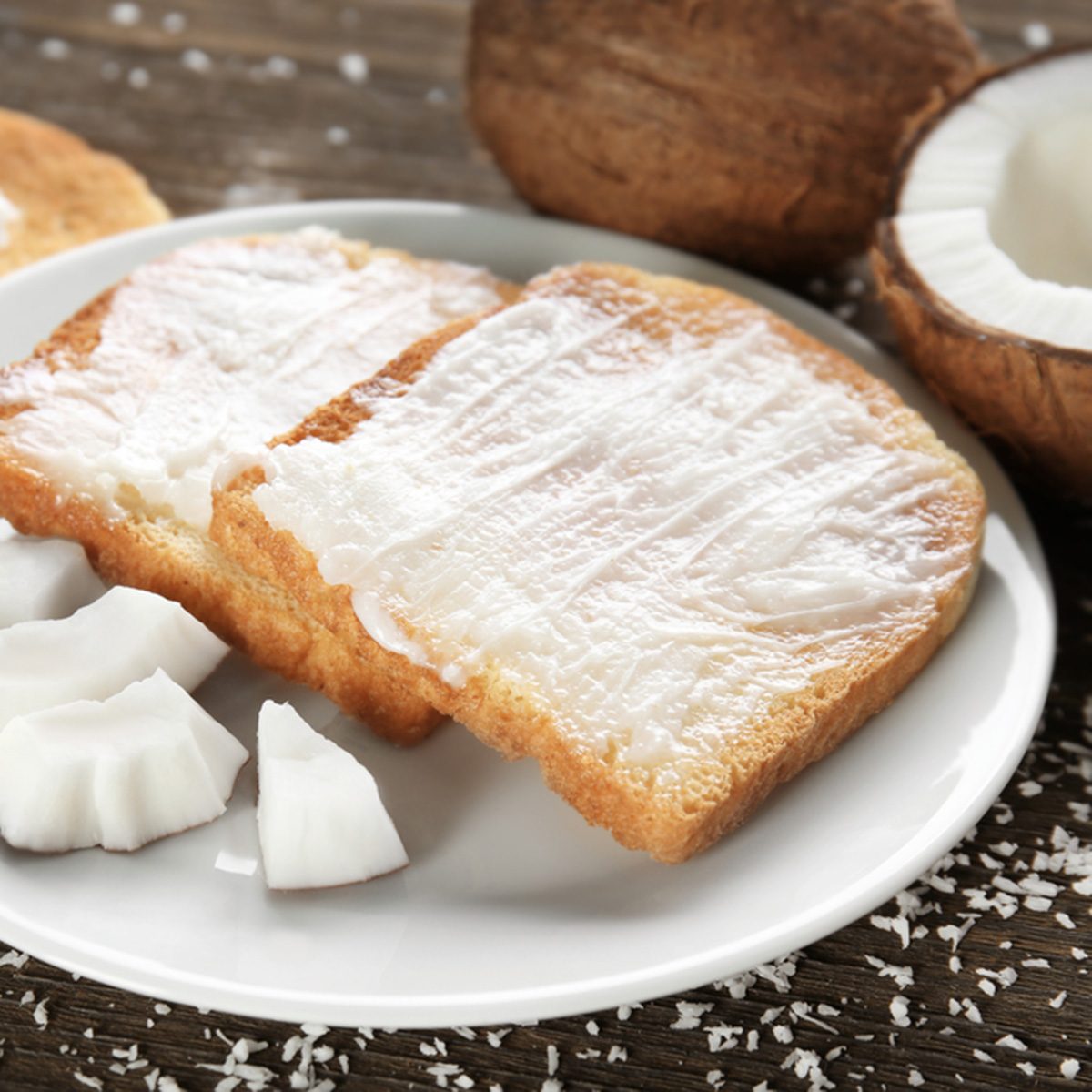Delicious toasts with coconut oil in plate on table
