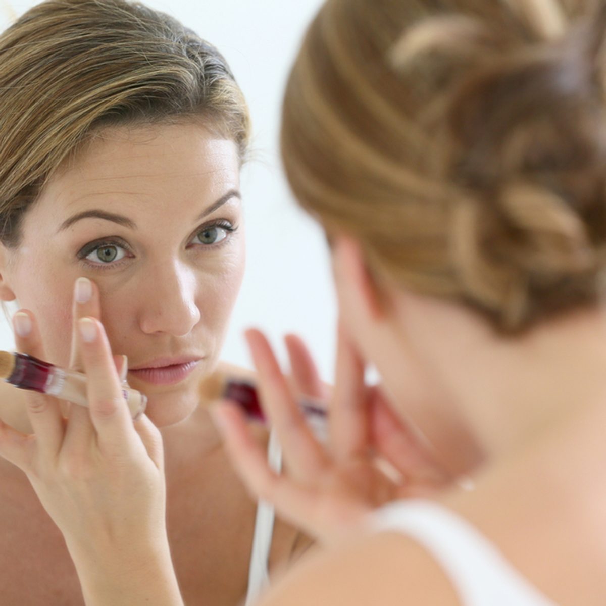 Beautiful blond woman applying concealer around eyes