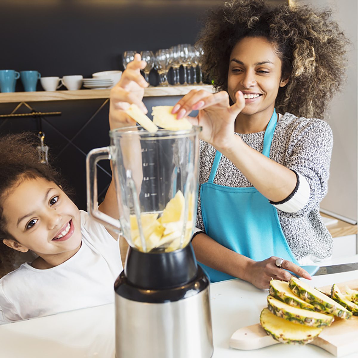 Beautiful African American woman and her daughter making a smoothie in the kitchen ;