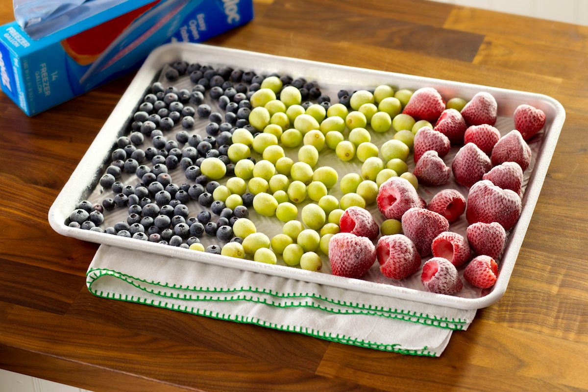 A baking sheet filled with froze blueberries, green grapes and strawberries.