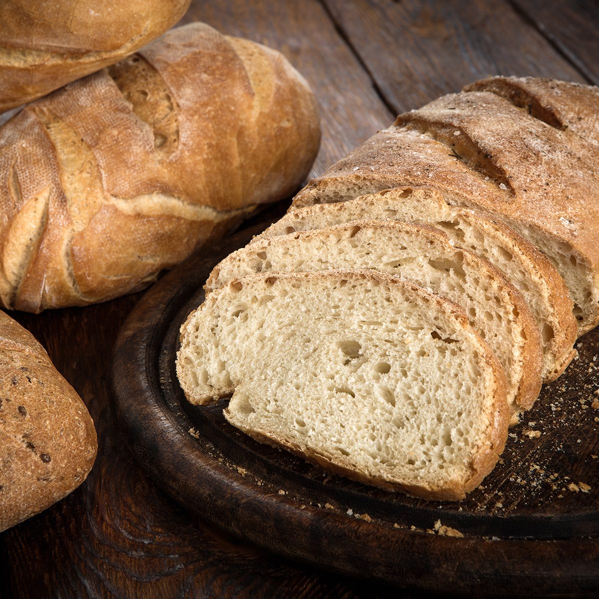 Yeast free, no knead, unleavened healthy organic rye wheat half sliced homemade bread loaf with sesame on a round desk at wooden table