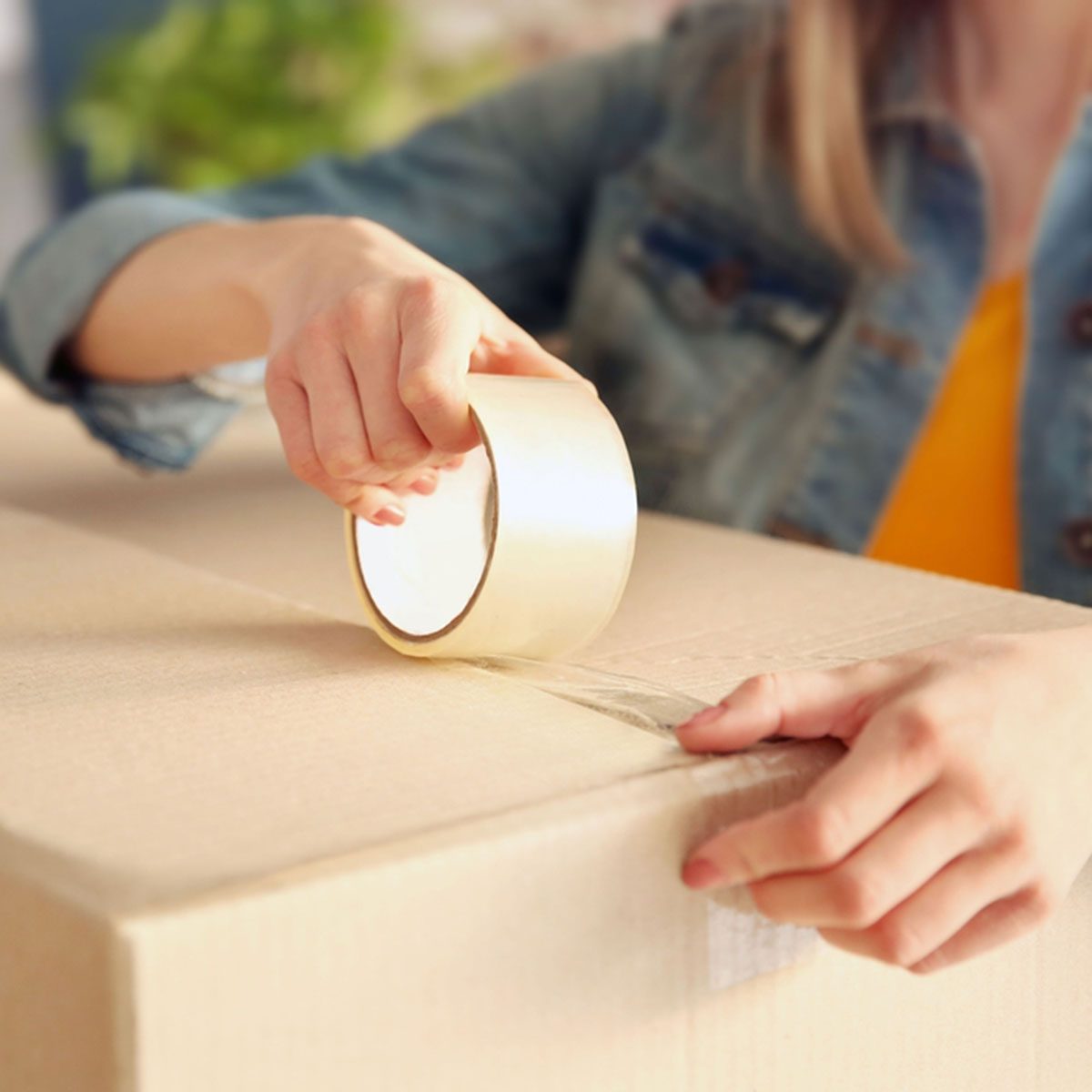 Young girl sealing with tape big cardboard box for moving