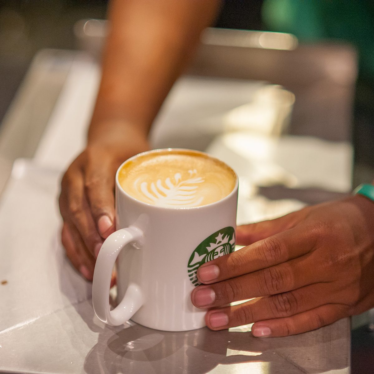 lose up of Starbucks Coffee Barista is hand over a coffee latte to the customers.