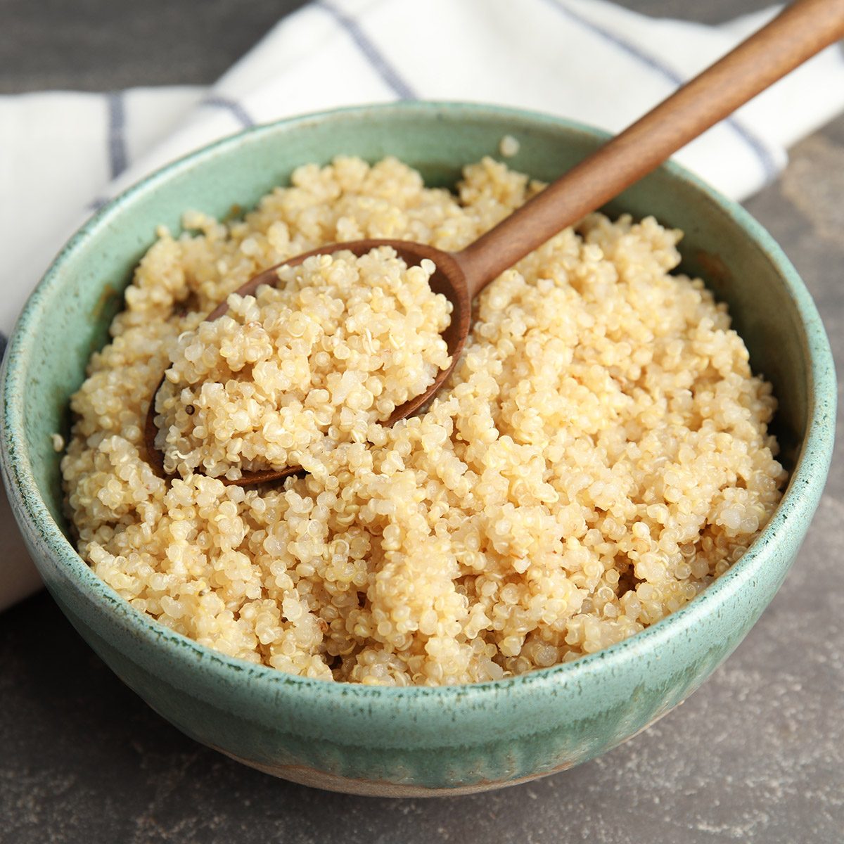 Composition with cooked quinoa in bowl and wooden spoon on table