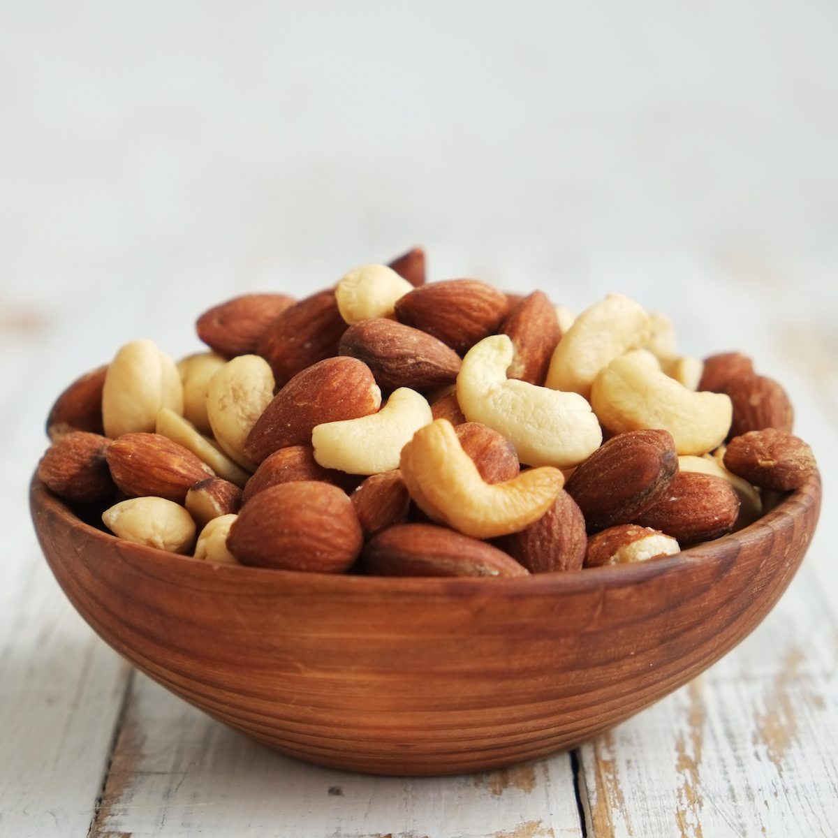 Mixed nuts in a  bowl on a white wooden background.