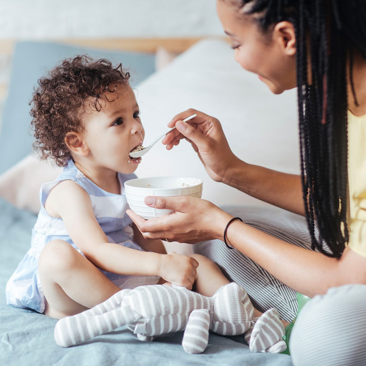 African woman giving her baby to eat and sitting in bedroom.