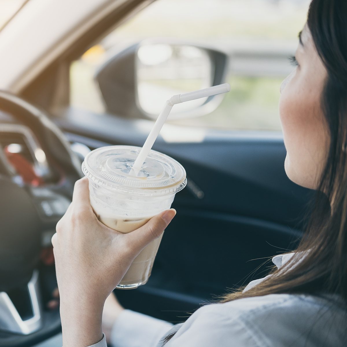 Asian woman holding iced coffee cup drinking while driving; Shutterstock ID 1030860874