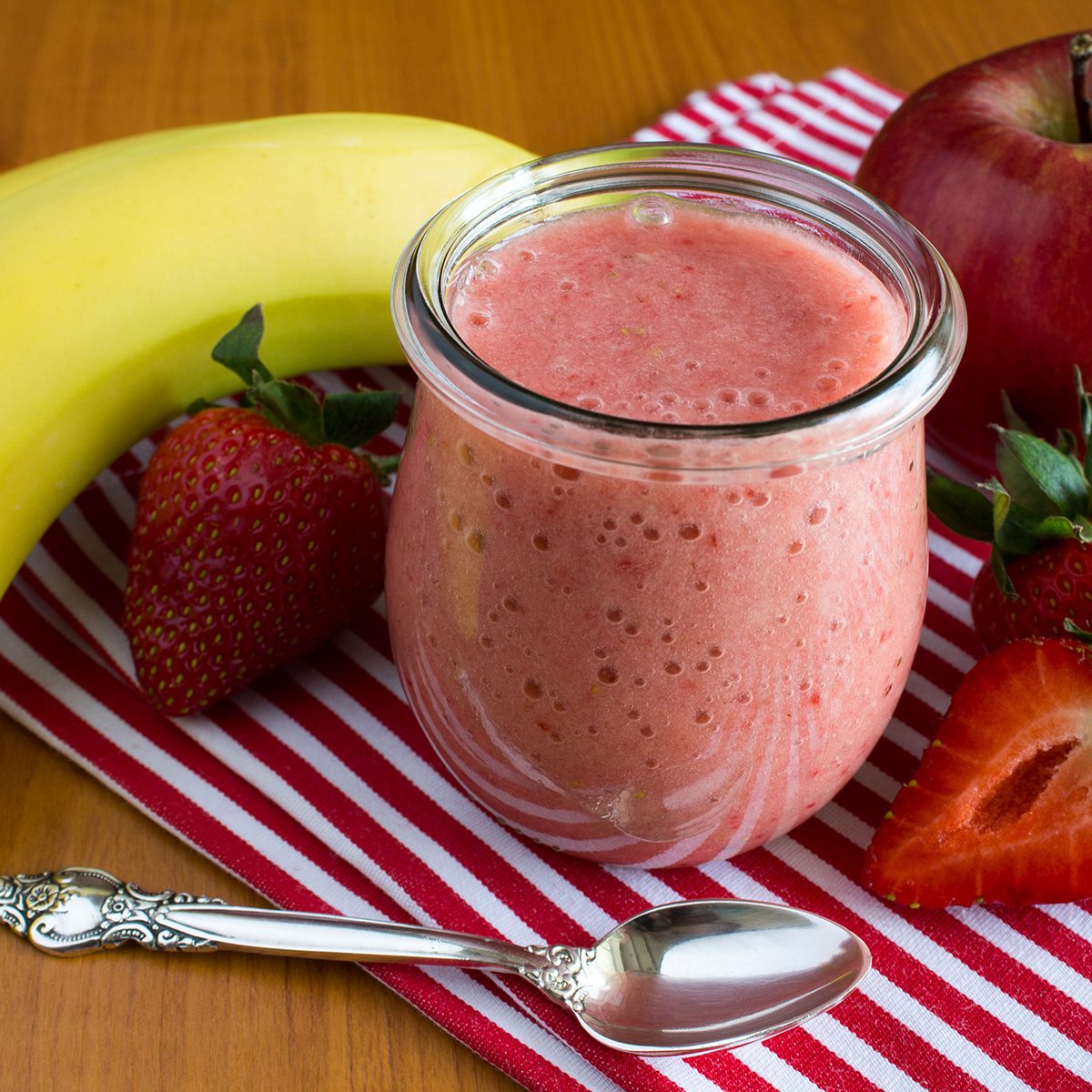 Puree with strawberry, banana and apple on the napkin on the wooden background