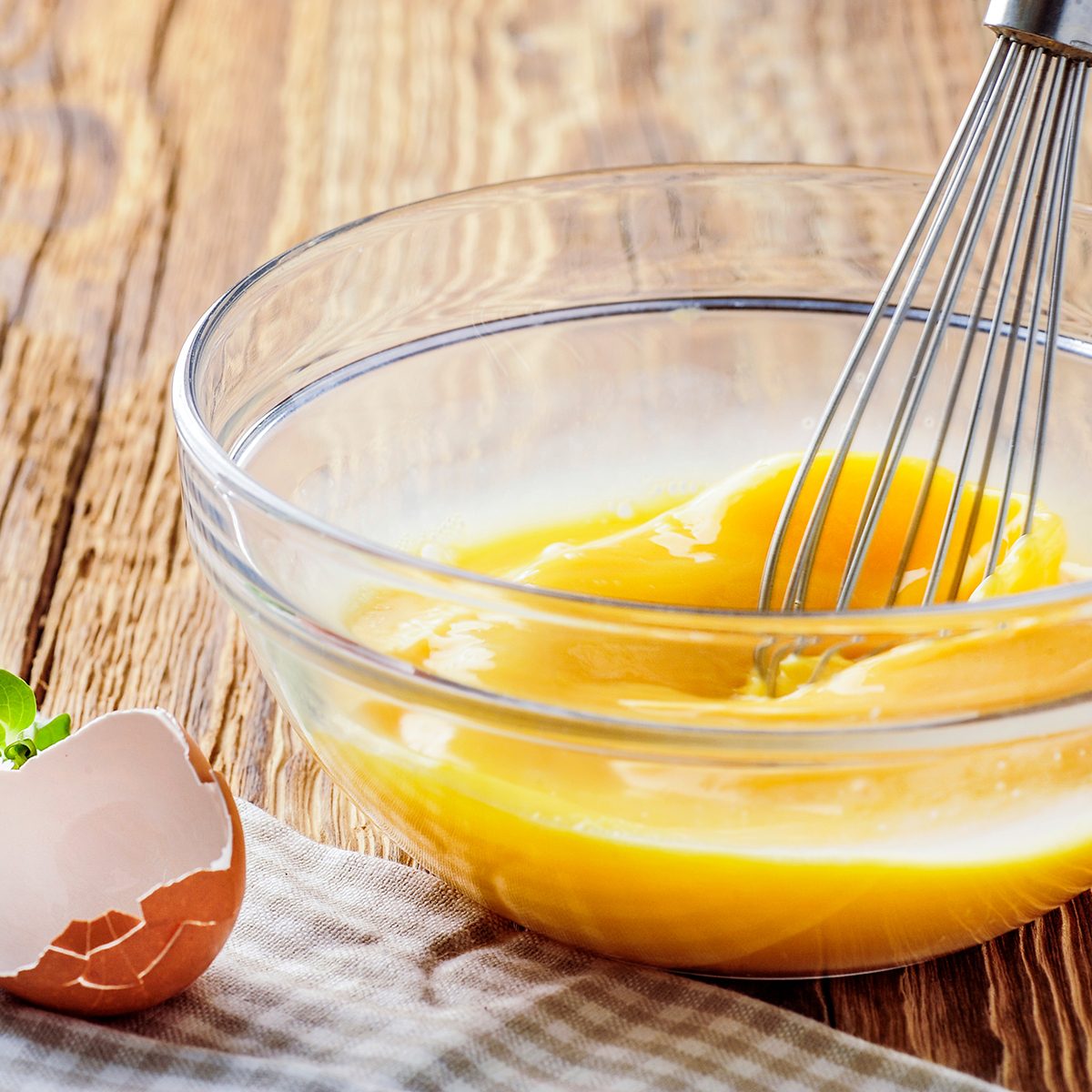 Woman whisking eggs. Wipped eggs in glass bowl with broken empty egg shell.
