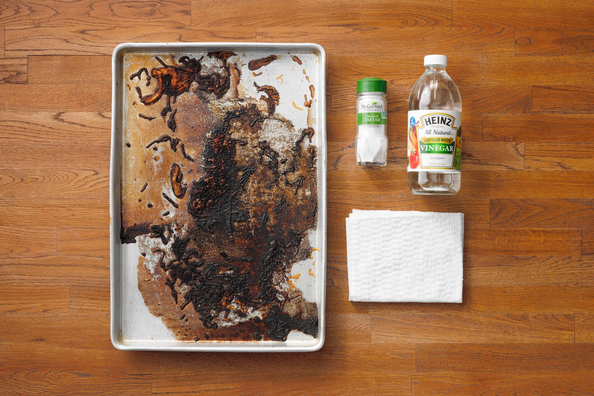 Dirty Baking Sheet next to cream of tartar, white vinegar, and a rag on wood butcher block background