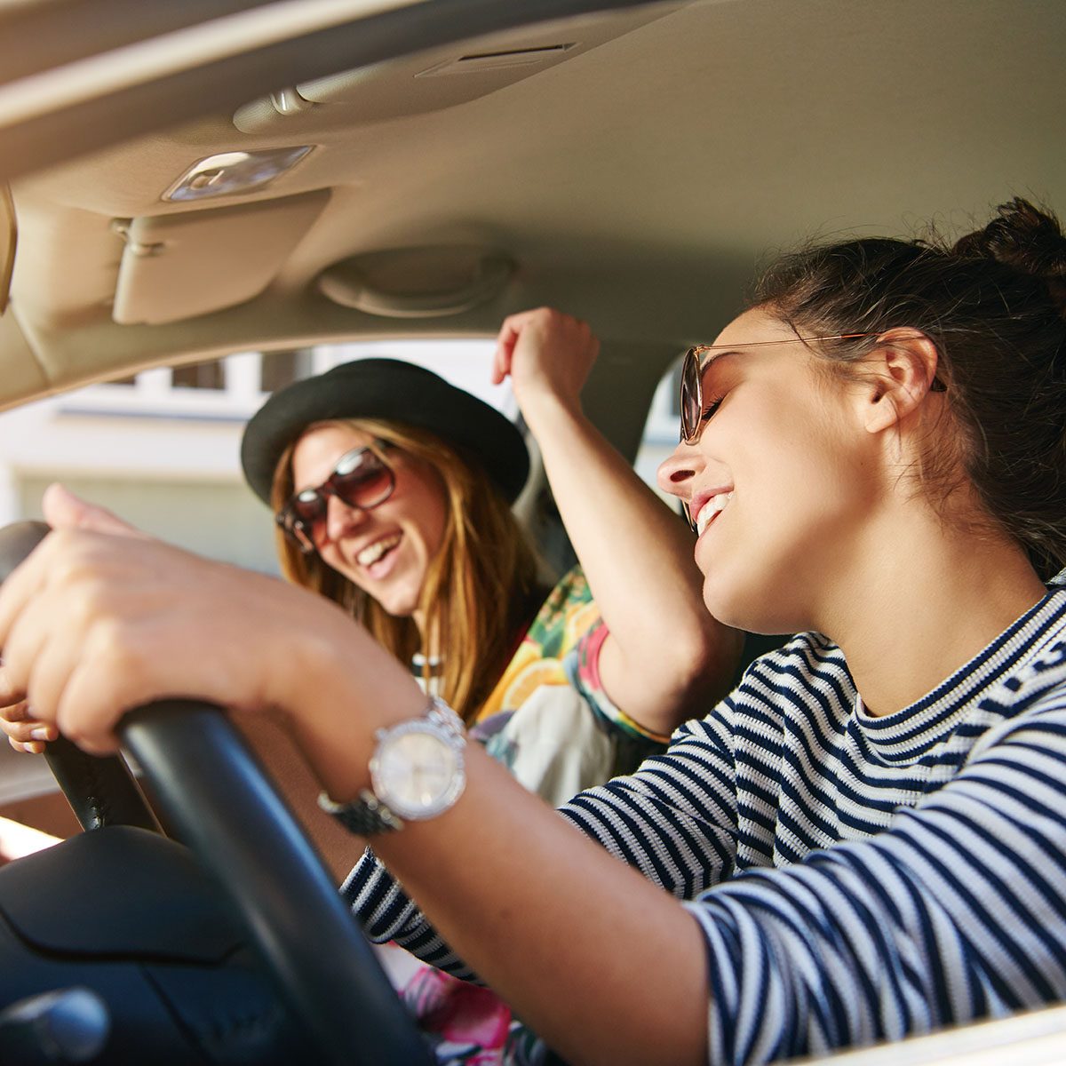 Two trendy attractive young woman singing along to the music as they drive along in the car through town viewed through the open side window