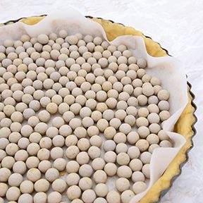 Close-up of pastry weights, ceramic beans, in an unbaked pie case lined with baking parchment;