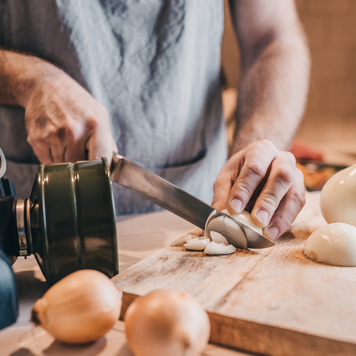 Rough male hands thinly chop the white onion with a knife on a wooden board - a gas mask from tears when cutting onions