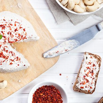 Vegan raw cheese from cashew nuts spread on the bread by knife on the white wooden background