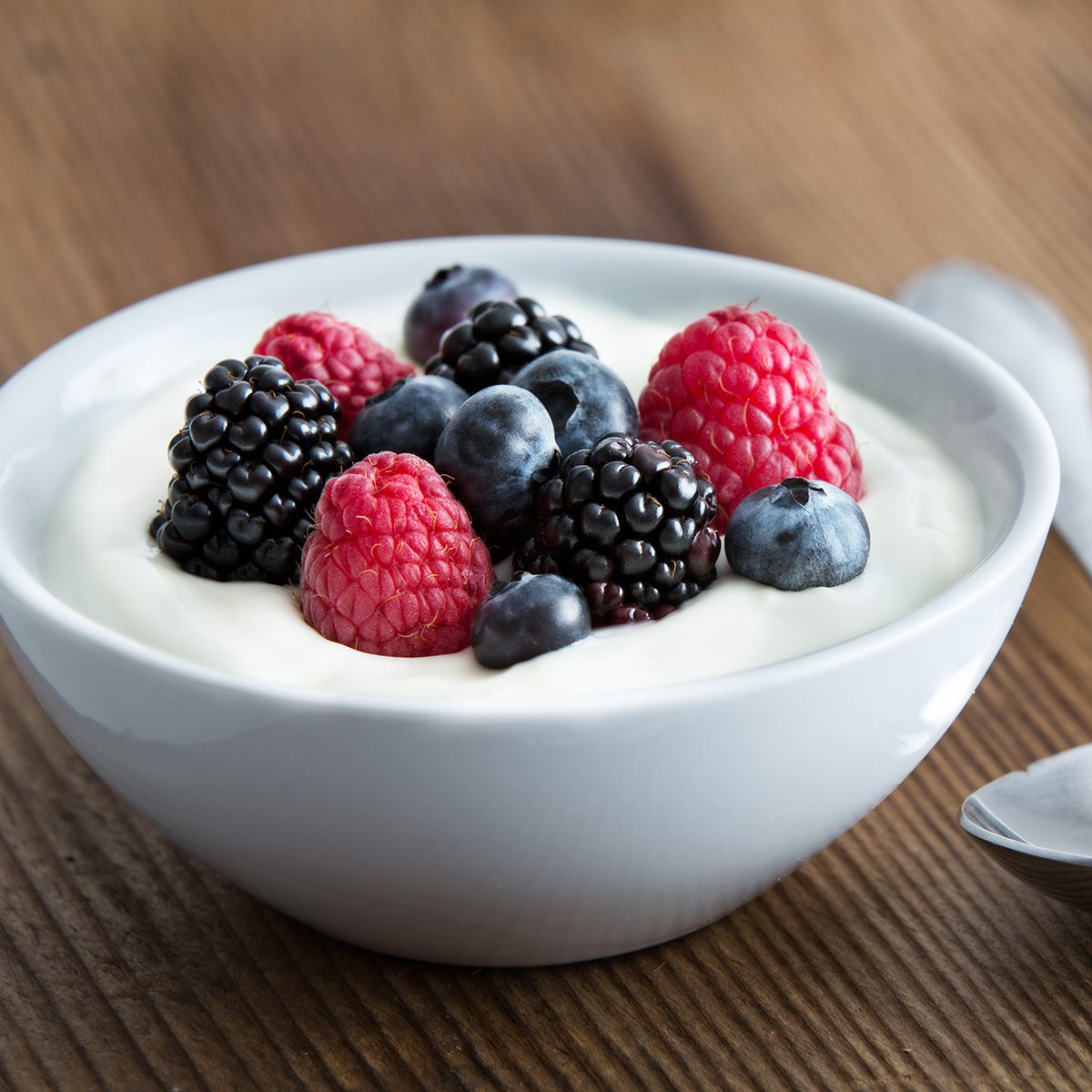 Bowl of fresh mixed berries and yogurt with farm fresh strawberries, blackberries and blueberries served on a wooden table