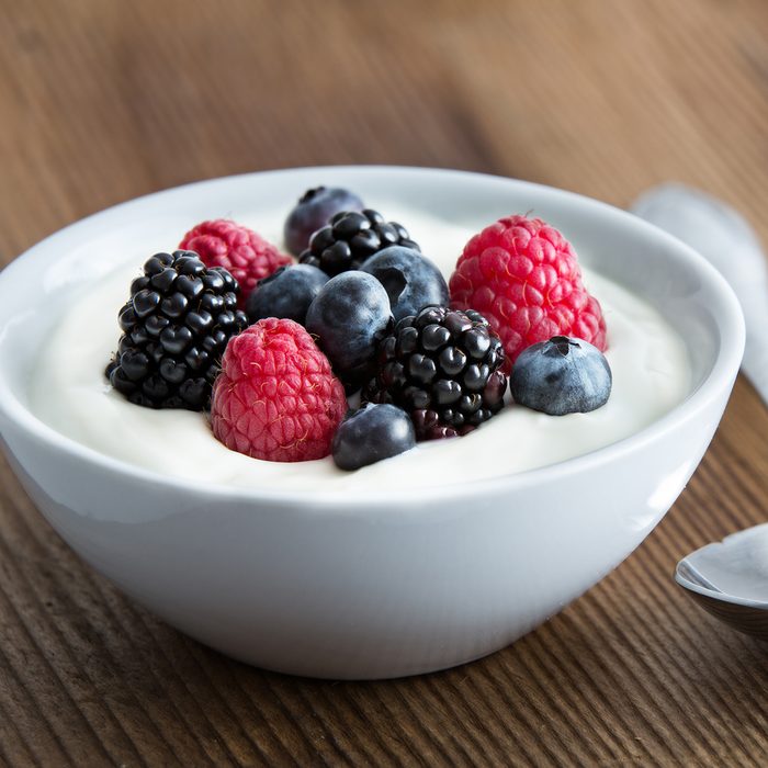Bowl of fresh mixed berries and yogurt with farm fresh strawberries, blackberries and blueberries served on a wooden table