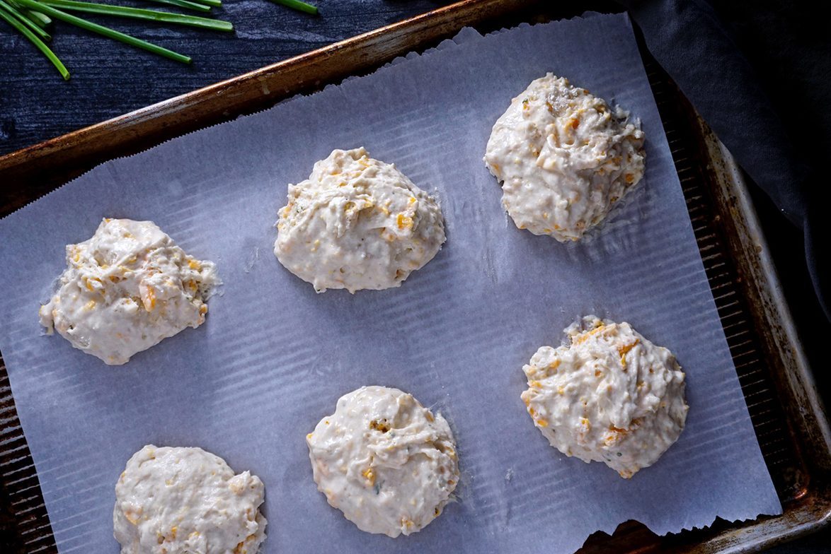 scooping heaping spoonfuls of cheddar bay biscuit dough onto lined baking sheet red lobster cheddar bay biscuits