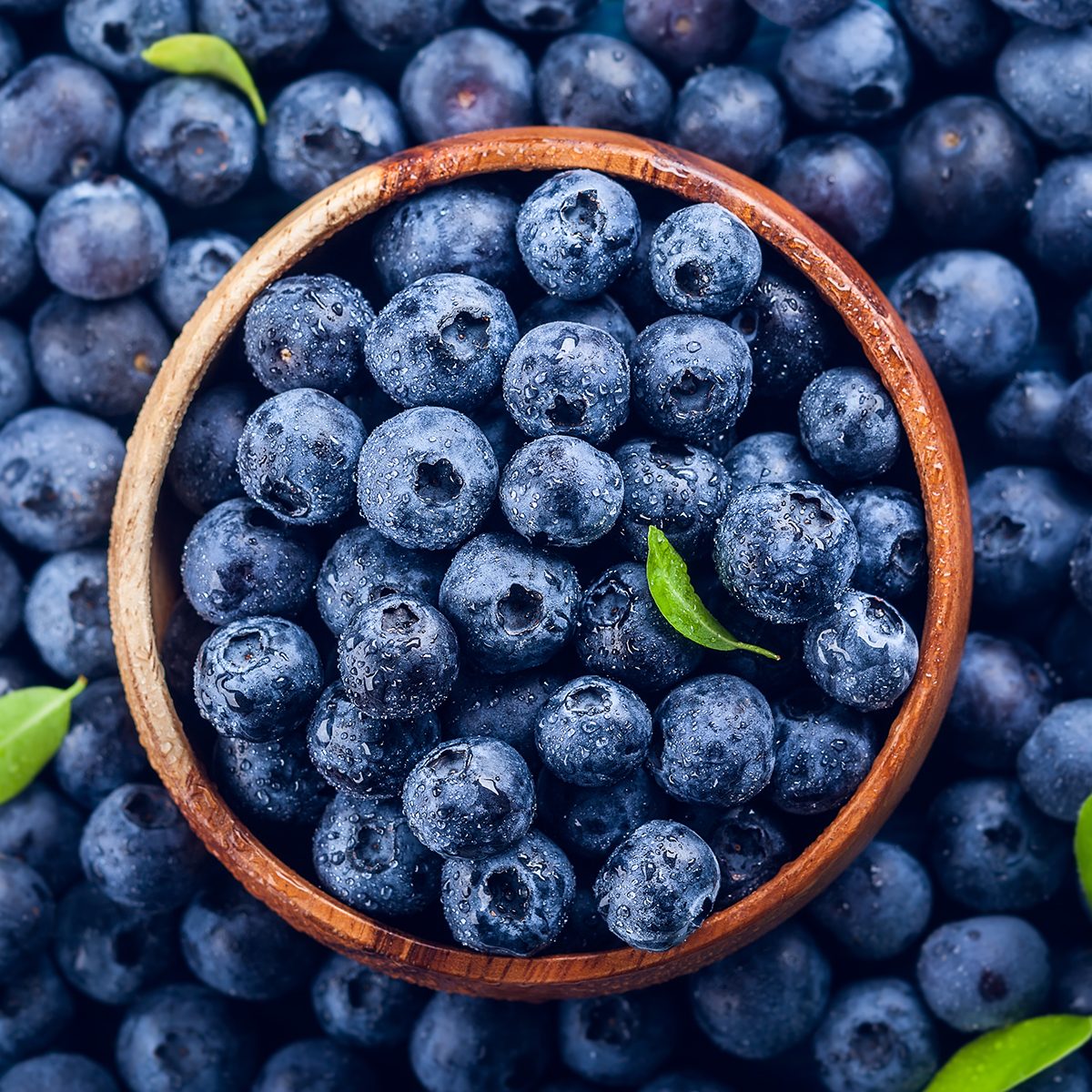 Fresh blueberry with drops of water in wooden bowl.
