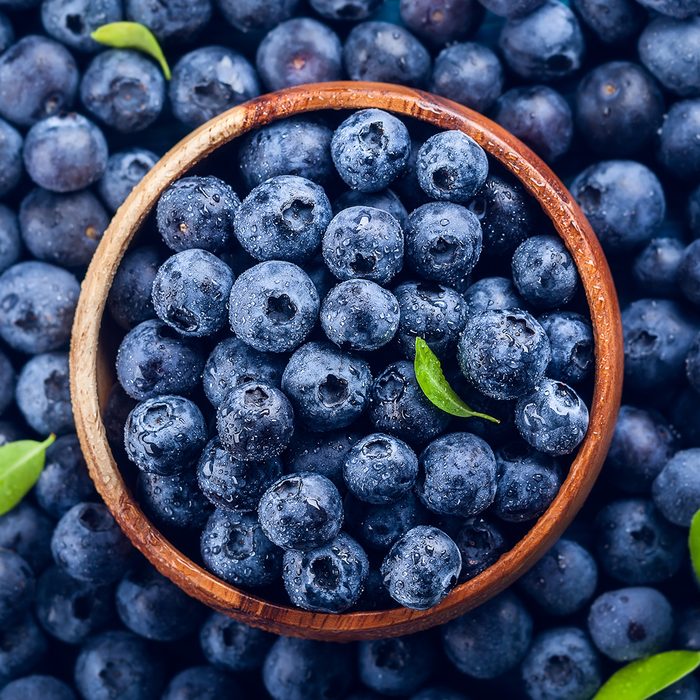 Fresh blueberry with drops of water in wooden bowl.