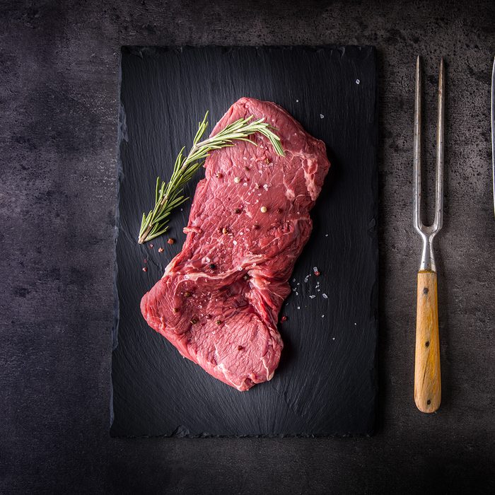 Beef raw rump steak with salt pepper rosemary butcher and fork.