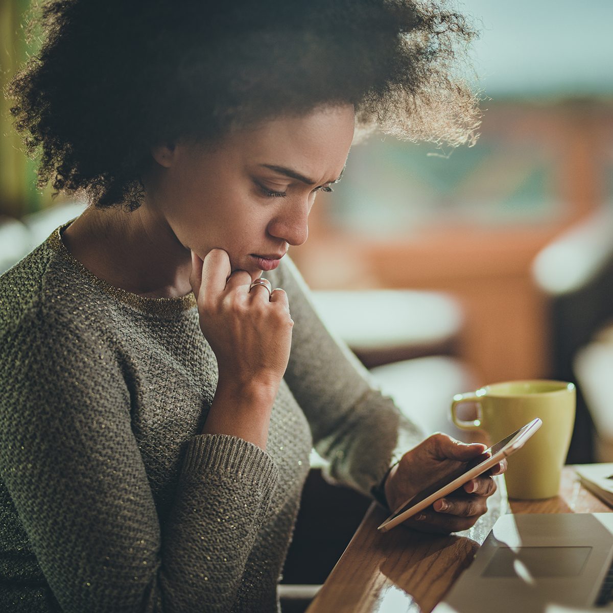 Young black woman reading a problematic text message on her mobile phone while working at home.