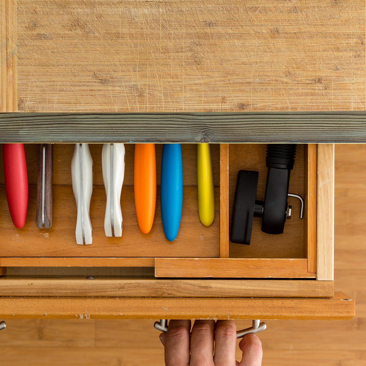 Man or chef opening a knife drawer in a kitchen in an overhead view of the neatly fitted interior of the drawer and a kitchen counter with cutting board