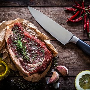 Raw beef steak on butchers paper with a kitchen knife at the right side shot from above on rustic wooden table.