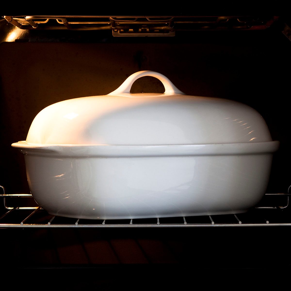 White porcelain baking dish with lid in open oven with light switch on