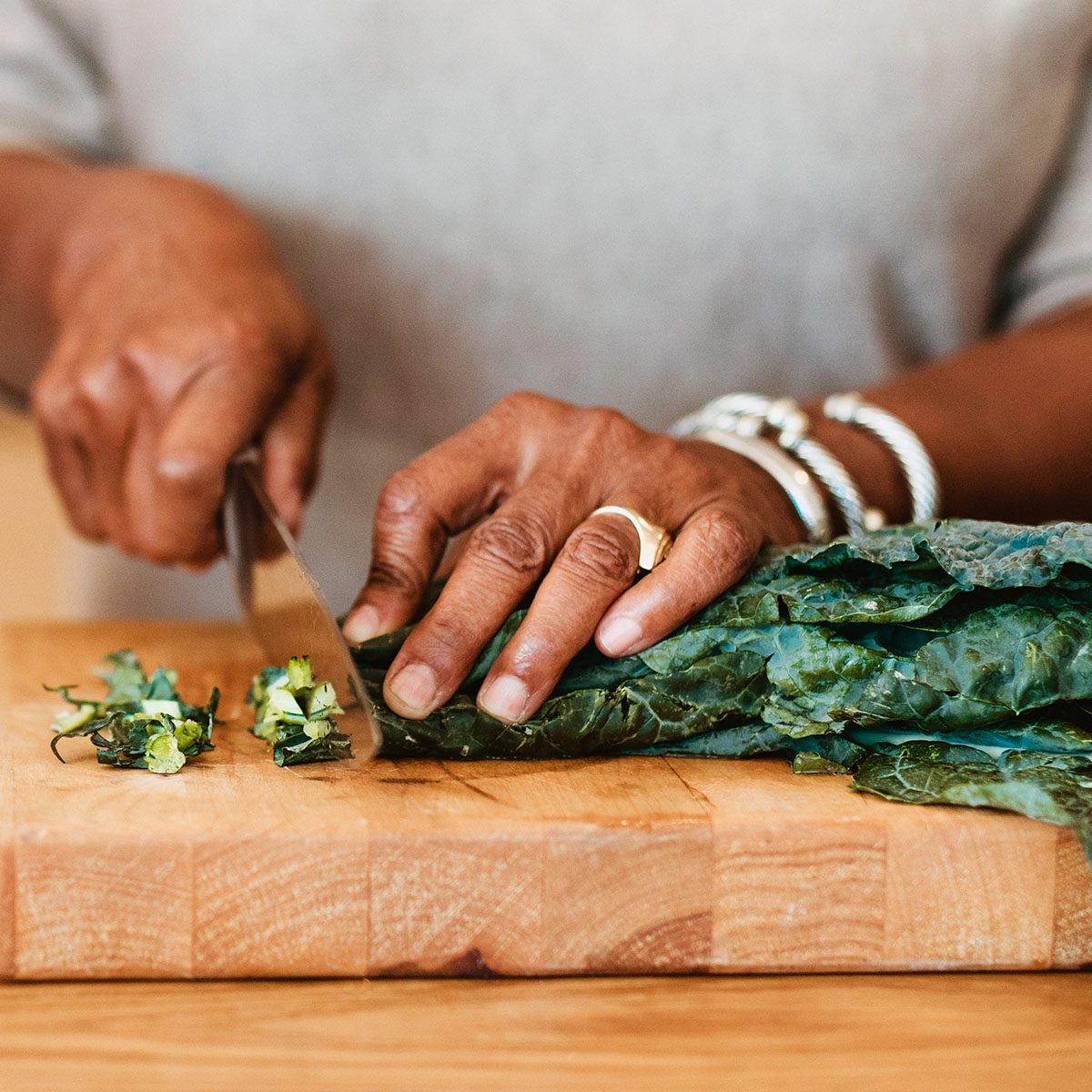 Midsection of woman chopping chard on cutting board. Female is preparing meal by husband at kitchen island. They are in kitchen together.